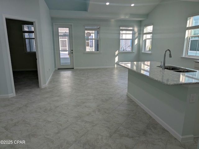 kitchen with baseboards, light stone counters, a sink, and recessed lighting