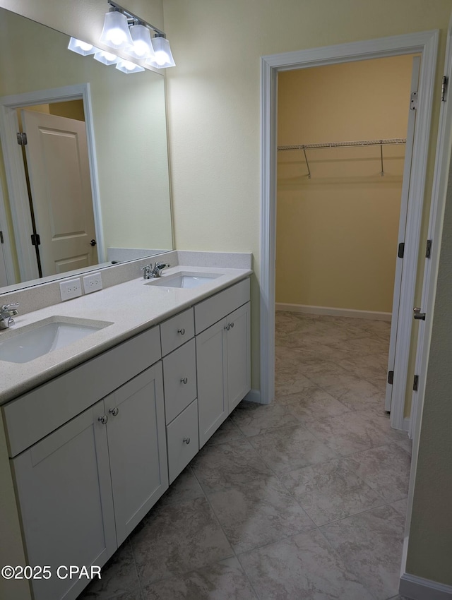 full bath with double vanity, a sink, a walk in closet, and baseboards