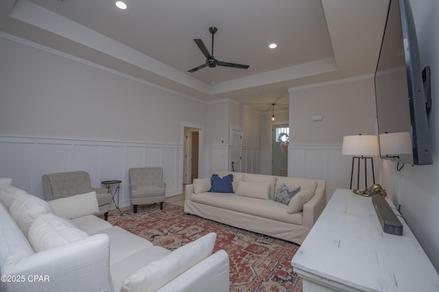 living room featuring recessed lighting, wainscoting, a ceiling fan, and a tray ceiling