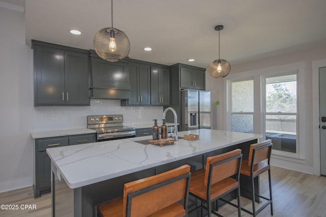 kitchen featuring light stone counters, light wood-style floors, appliances with stainless steel finishes, decorative backsplash, and custom exhaust hood