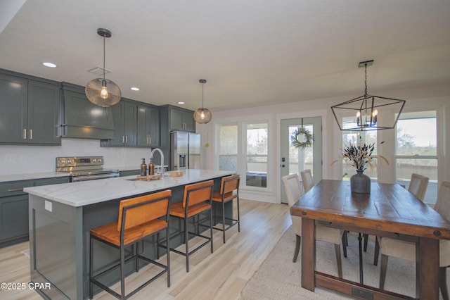 kitchen with light stone countertops, an island with sink, a sink, appliances with stainless steel finishes, and light wood-type flooring