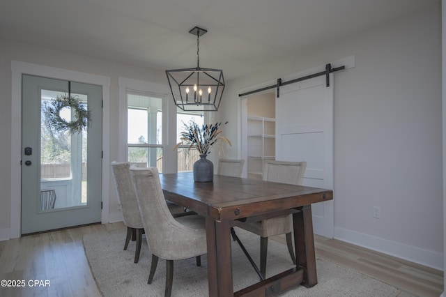 dining space with a barn door, baseboards, light wood-style floors, and an inviting chandelier