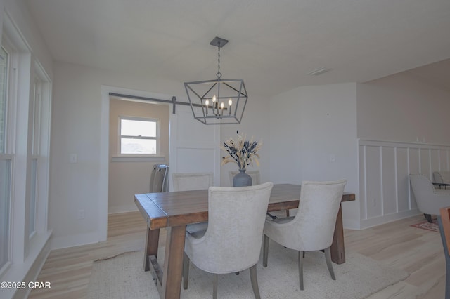 dining area with a chandelier, a decorative wall, light wood-type flooring, and a barn door