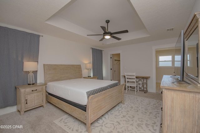 bedroom with light carpet, visible vents, a raised ceiling, and ceiling fan