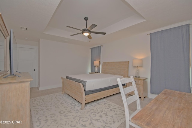 bedroom with a ceiling fan, baseboards, visible vents, a tray ceiling, and light carpet