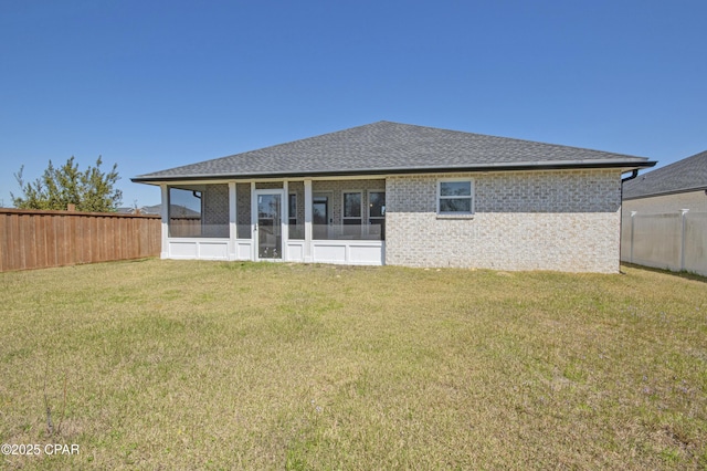 rear view of house featuring a shingled roof, a lawn, a fenced backyard, and a sunroom