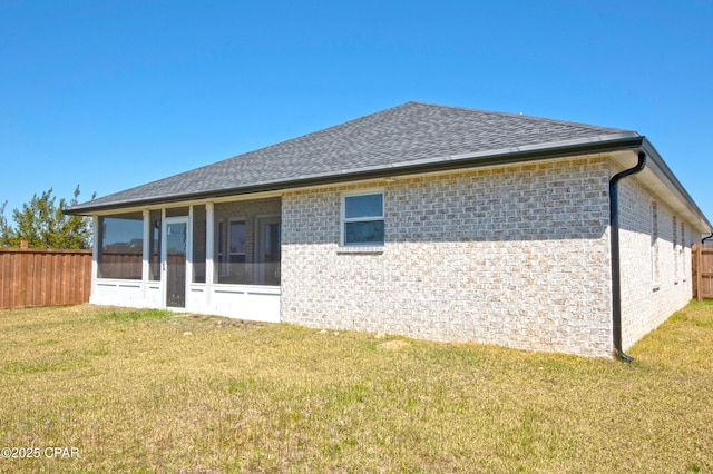 rear view of property featuring fence, a lawn, roof with shingles, and a sunroom