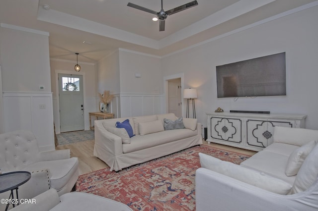 living room with a tray ceiling, a ceiling fan, light wood-type flooring, and wainscoting