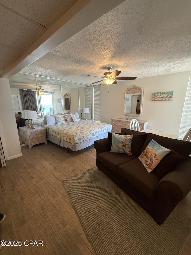 bedroom with baseboards, a textured ceiling, ceiling fan, and wood finished floors