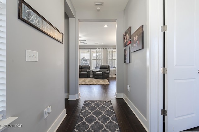 corridor with visible vents, baseboards, and dark wood-style flooring