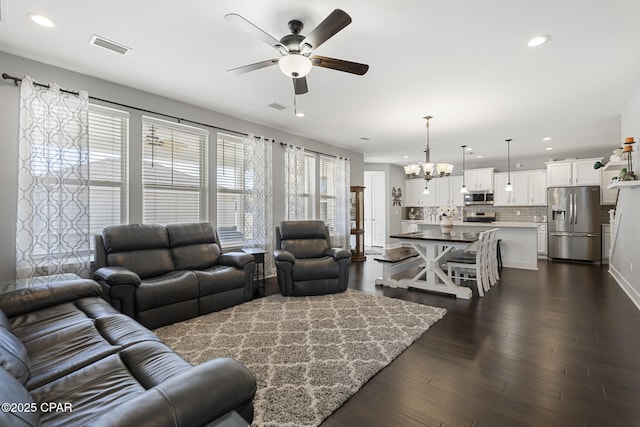 living area featuring dark wood-style floors, ceiling fan with notable chandelier, visible vents, and recessed lighting