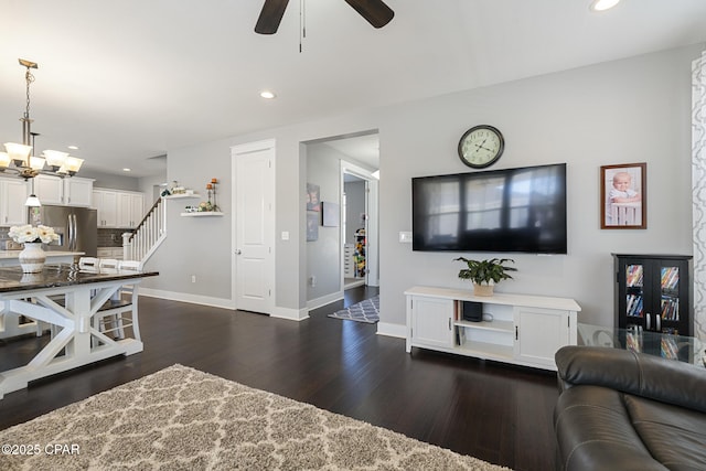 living area featuring recessed lighting, ceiling fan with notable chandelier, dark wood-type flooring, baseboards, and stairway