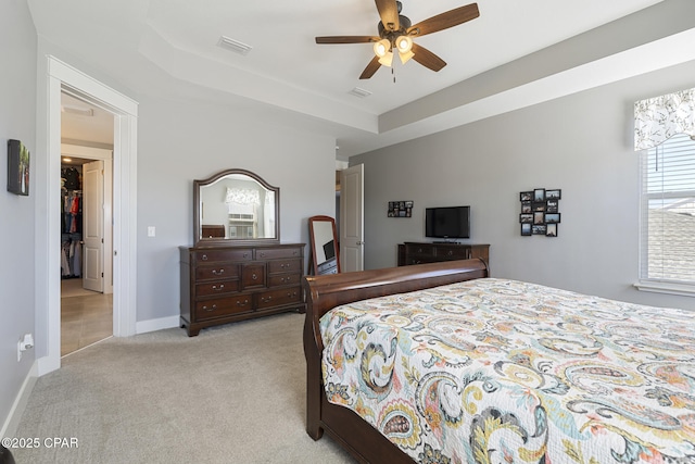 bedroom with a tray ceiling, light carpet, visible vents, and baseboards