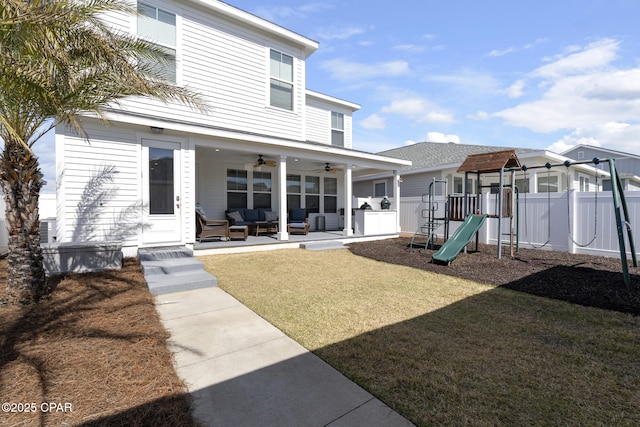 back of property featuring a ceiling fan, a playground, fence, and a lawn