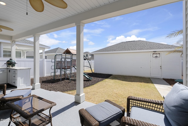 view of patio featuring a playground, grilling area, fence, ceiling fan, and an outdoor structure