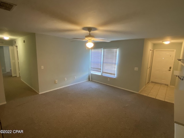 empty room with visible vents, baseboards, ceiling fan, light colored carpet, and light tile patterned floors