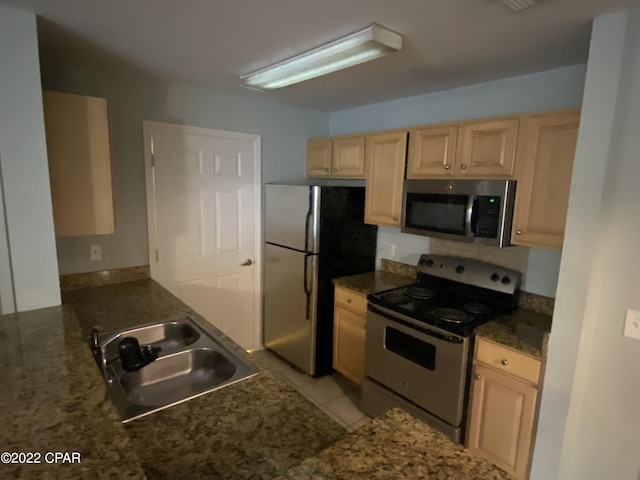 kitchen featuring light brown cabinets, dark stone counters, light tile patterned floors, appliances with stainless steel finishes, and a sink