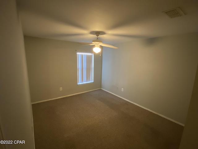 spare room featuring visible vents, baseboards, a ceiling fan, and dark colored carpet