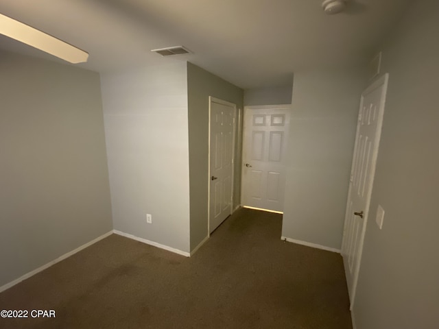 hall featuring visible vents, baseboards, and dark carpet