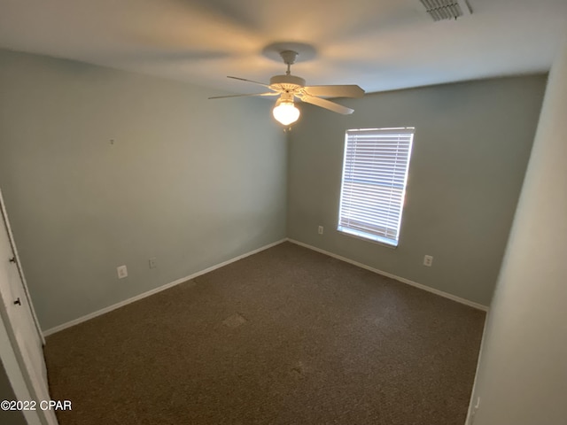 empty room featuring a ceiling fan, visible vents, dark carpet, and baseboards