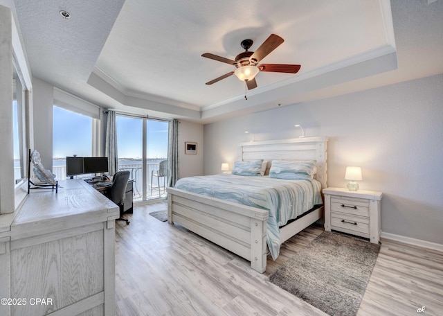 bedroom with baseboards, a tray ceiling, access to exterior, crown molding, and light wood-type flooring