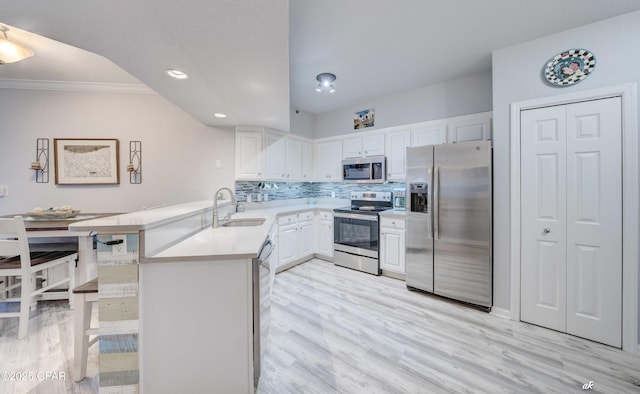 kitchen with a peninsula, stainless steel appliances, light countertops, white cabinets, and backsplash