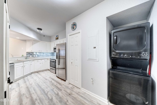 kitchen featuring stacked washer and dryer, electric panel, backsplash, stainless steel appliances, and white cabinets