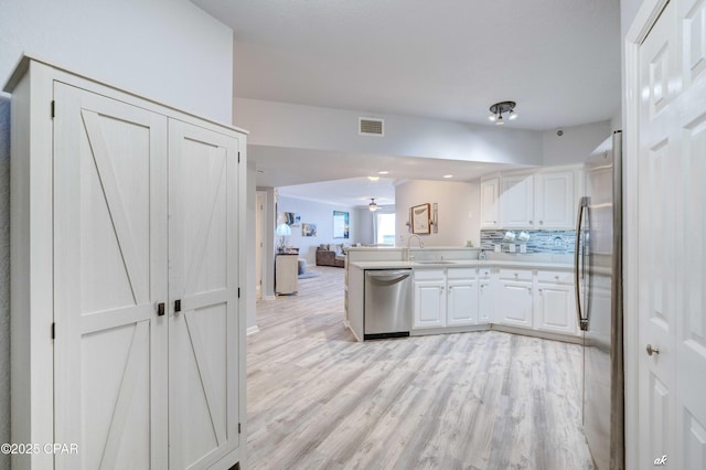 kitchen featuring open floor plan, light wood-style floors, appliances with stainless steel finishes, a peninsula, and white cabinets