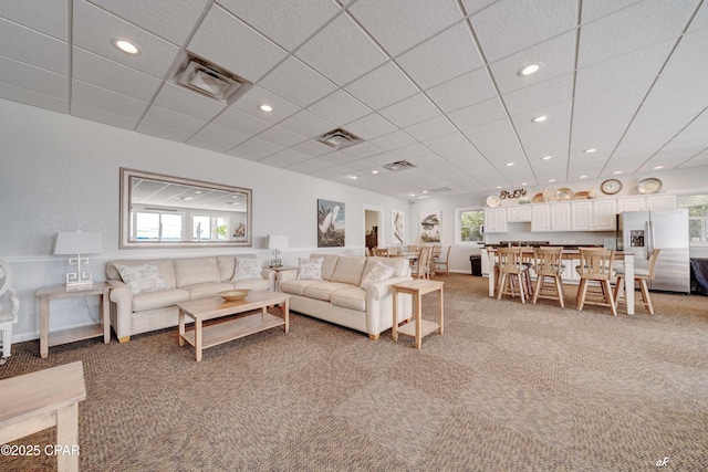 living area with a wealth of natural light, visible vents, and light colored carpet