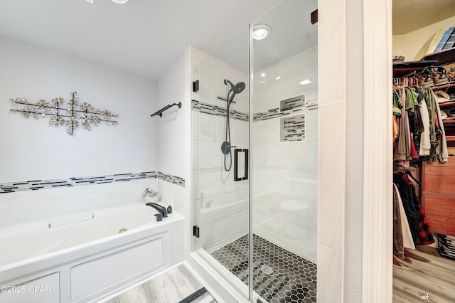 full bath featuring a spacious closet, a shower stall, a garden tub, and wood finished floors