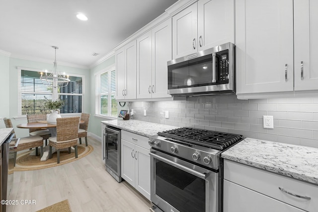 kitchen featuring tasteful backsplash, wine cooler, ornamental molding, stainless steel appliances, and white cabinetry