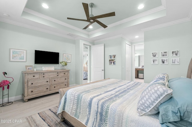 bedroom featuring light wood-style flooring, ensuite bathroom, a tray ceiling, crown molding, and baseboards