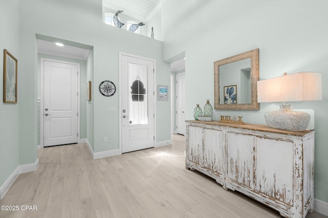 foyer with light wood-style flooring, a high ceiling, and baseboards