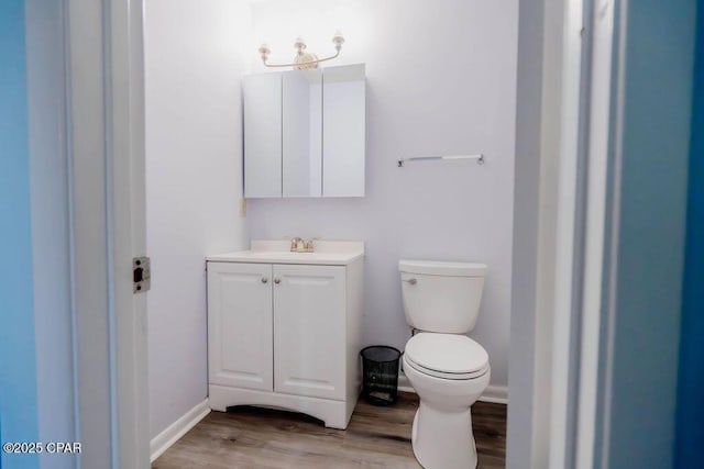 half bathroom featuring vanity, toilet, wood finished floors, and baseboards