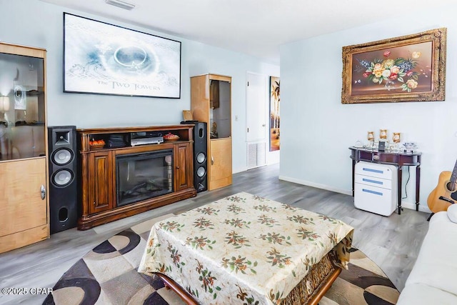 living room featuring a glass covered fireplace, wood finished floors, visible vents, and baseboards