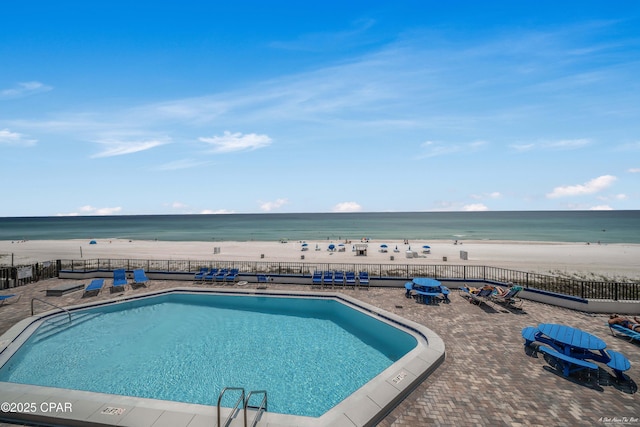 community pool with a patio, fence, and a beach view