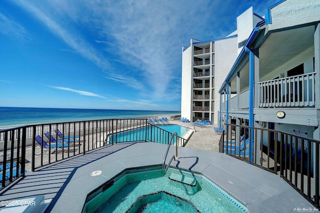 pool featuring a beach view, a patio area, a water view, and a hot tub