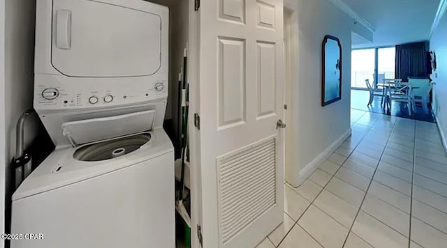 laundry room featuring laundry area, light tile patterned flooring, baseboards, and stacked washer and clothes dryer