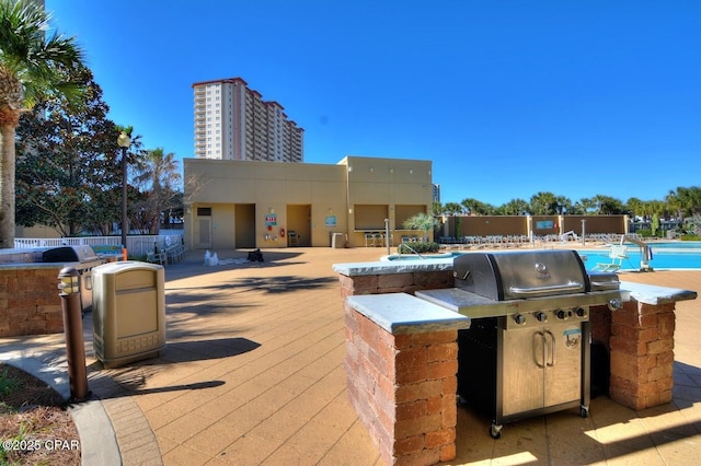 view of patio / terrace with grilling area, an outdoor kitchen, a community pool, and fence