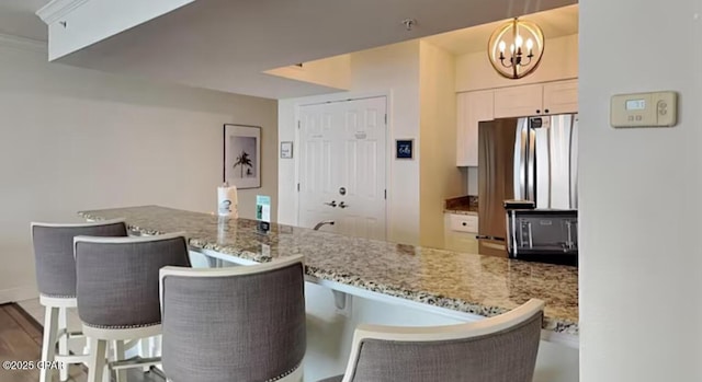 kitchen featuring light stone counters, wood finished floors, freestanding refrigerator, white cabinetry, and a notable chandelier