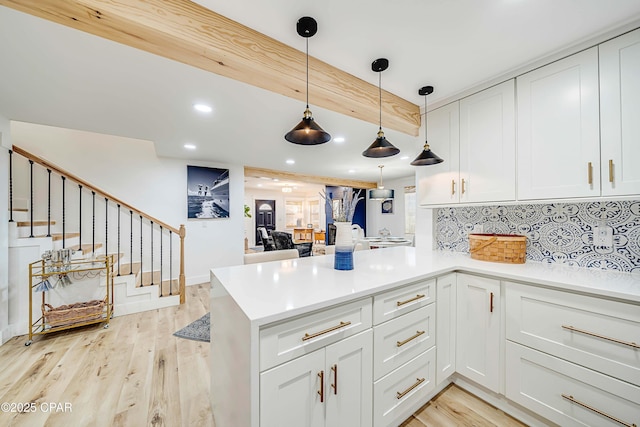 kitchen featuring a peninsula, light wood finished floors, tasteful backsplash, and white cabinetry