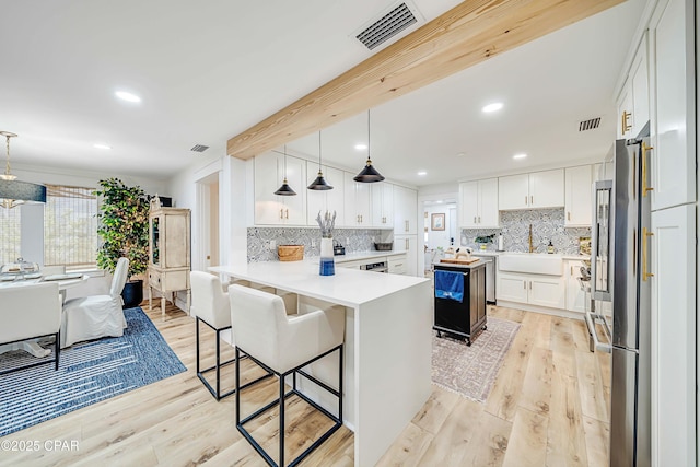 kitchen with visible vents, light wood-style flooring, white cabinets, a peninsula, and a kitchen breakfast bar