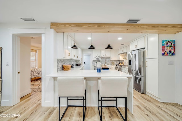 kitchen featuring a breakfast bar area, stainless steel appliances, a peninsula, visible vents, and light wood-style floors