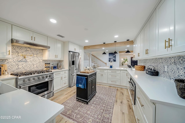 kitchen featuring premium appliances, light countertops, a peninsula, light wood-type flooring, and under cabinet range hood