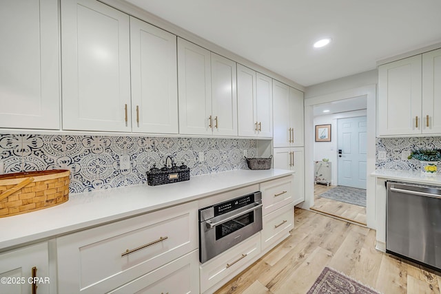 kitchen featuring light wood finished floors, stainless steel appliances, light countertops, decorative backsplash, and white cabinetry