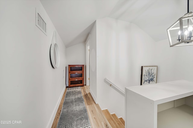 hallway with baseboards, visible vents, vaulted ceiling, an upstairs landing, and light wood-type flooring