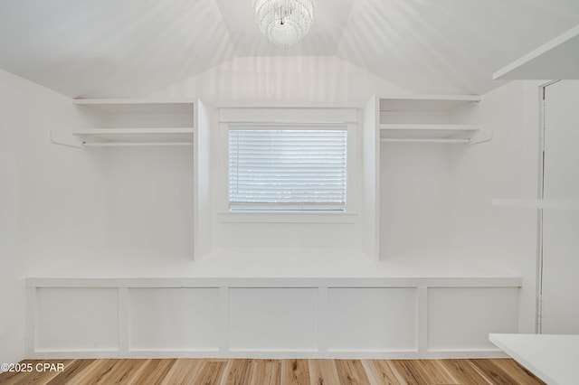 walk in closet with a chandelier, light wood-type flooring, and vaulted ceiling