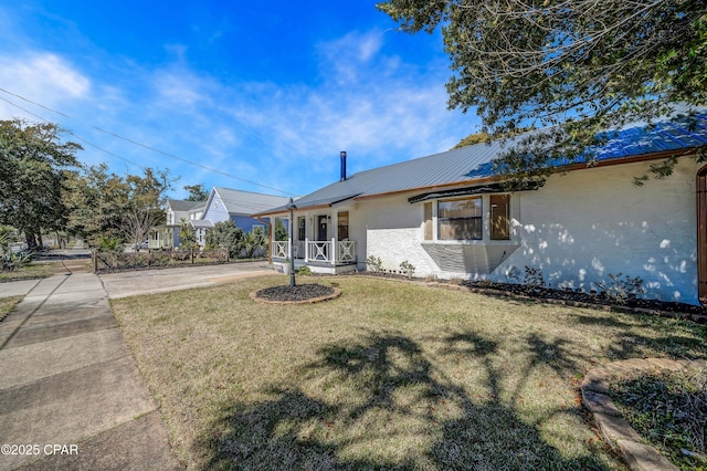 single story home with a front yard, covered porch, metal roof, and stucco siding