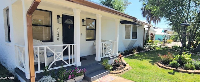 doorway to property featuring a porch, a lawn, and stucco siding