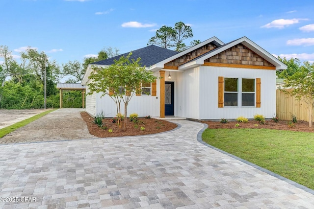 view of front of home with a front yard, decorative driveway, fence, and a shingled roof